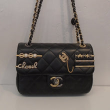 Load image into Gallery viewer, This Chanel Vintage Clips Flap Embellished has the diamond stitched pattern. It has a number of gold and silver charms on the bag some of which are: Chanel, Paris and the Chanel logo. The double shoulder chain is gold with a strip of leather woven between the links. It has a silver medallion attached to the shoulder chain which has the word Paris with an address. The interior of this bag is satin white.