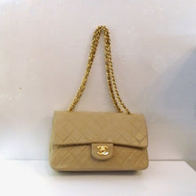Load image into Gallery viewer, This Chanel Vintage Double Flap 255 has the diamond stitched pattern with 24 karat gold plated hardware. It has a double gold chain carrying handle with a leather strip running through the links of the chain. The front latch is the CC logo in gold hardware. This bag has a pocket on the outside back of the bag. The interior is in the same beige color as the outside with an inside pocket. The outside of the bag has a slight color transfer.
