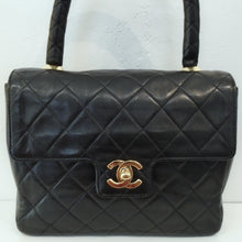 Load image into Gallery viewer, This Chanel Lambskin Top Handle is black with 24 Karat Gold Hardware which includes the Chanel Logo on the front lip of the bag. The interior is red with a zippered pocket.