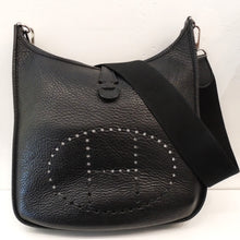Load image into Gallery viewer, This Hermes Black Evelyne Clemence Leather PM has silver hardware and a wide sturdy canvas shoulder strap. It has a small strap at the top of the bag that pulls the top together, a pocket in the back that also has a strap snap closure. The interior of the bag is the inner side of the leather. This bag is somewhat soft with a pebbled appearance.