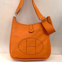 Load image into Gallery viewer, This Hermes Vintage Orange Clemence Leather Evelyn PM has silver hardware and the sturdy canvas (guitar strap) shoulder strap. The front of the bag has the Hermes Logo perforations.