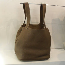 Load image into Gallery viewer, This Hermes Vintage Picotin 18 Etoupe Clemence Leather bag has two long loop handles at the top of the bag made from the same leather as the bottom of the bag. It has a seam on the side of the bag and 4 metal studs on the bottom of the bag. The interior of the bag is the same shade of camel.