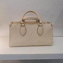 Load image into Gallery viewer, This Louis Vuitton Vintage Empreinte Leather On The Go East/West has the large monogram pattern embossed in the leather and gold hardware. It has two carrying handles and also includes a detachable leather and chain strap. It has a zippered inside pocket with a pocket on either side. The interior of this bag is also a cream color.