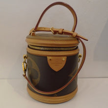 Load image into Gallery viewer, This Louis Vuitton Vintage Reverse Monogram Cannes Vanity is in a cylinder shape with large monogram on sides and top of the bag. The background of the bag is dark brown and has camel trim including the straps. It includes an adjustable, detachable strap (also in camel), a lock & key and a dust bag. The interior of this bag is black.
