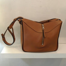 Load image into Gallery viewer, This Loewe Cognac Hammock Bag is a dark camel color with a shoulder strap and front zipper that zips in center from top to bottom. The interior of this bag is black.

