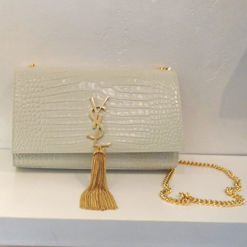 This YSL Cream Crocodile Embossed Kate Tassel Bag has a gold tassel attached to the gold YSL logo on the front of the bag. The interior of this bag is black.