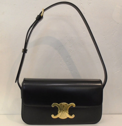 This Celine Claude Shoulder Bag is black with a black shoulder strap and gold hardware. The front latch is the Celine logo with Celine & Paris engraved on it. The interior of this bag is also black.