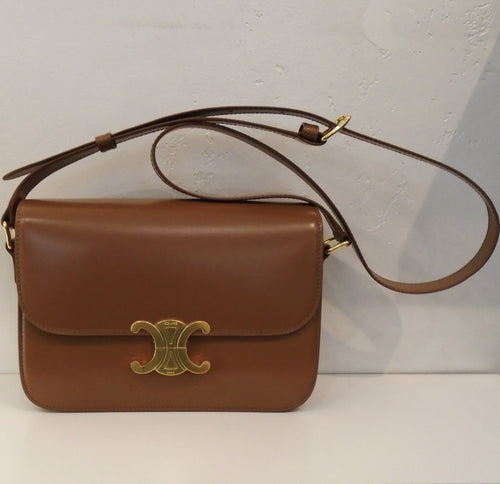 This Celine Classique Triomphe is tan with gold hardware and a  tan shoulder strap. The gold front closure is the Celine logo with the words Celine and Paris engraved on it. The interior of this bag is also tan.