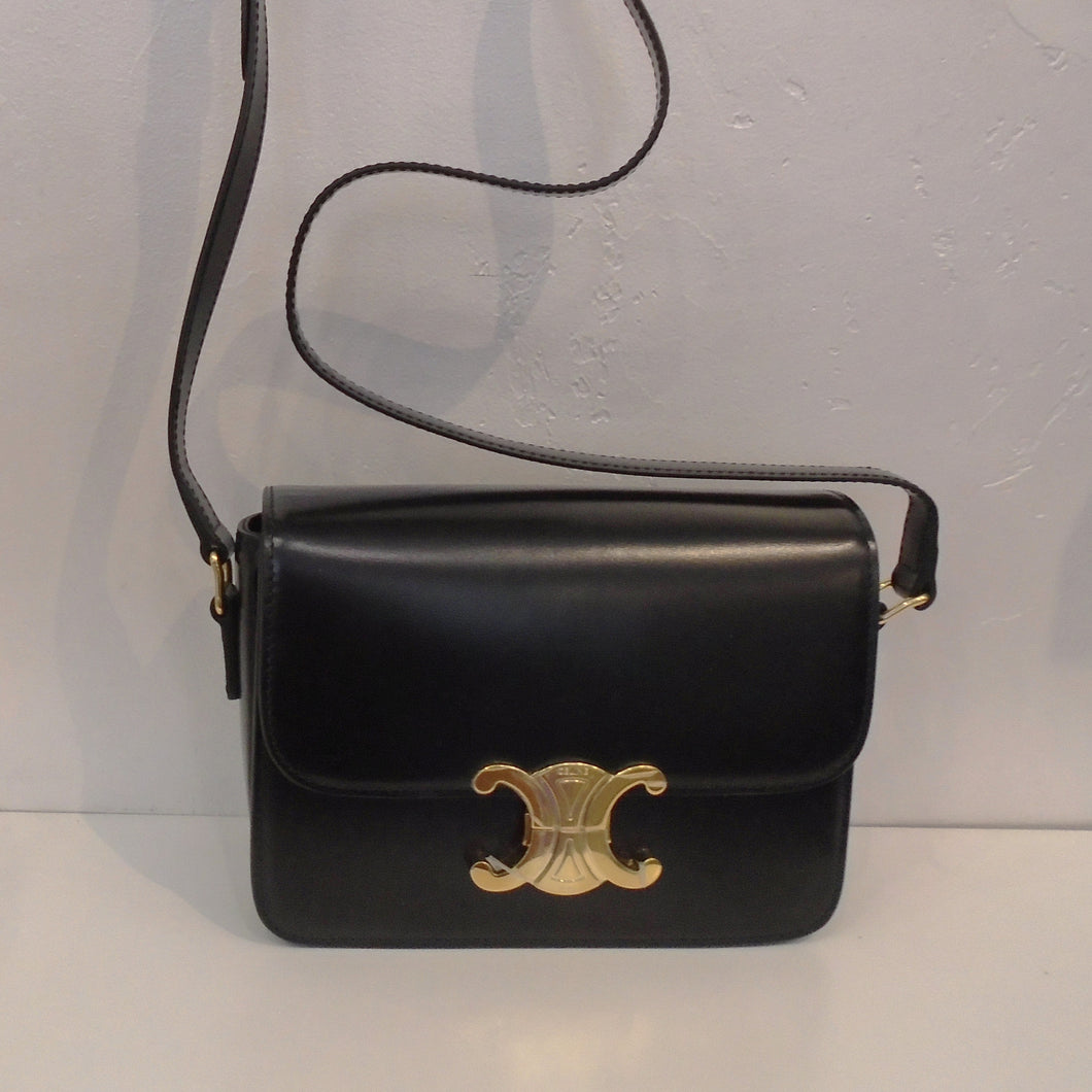 This Celine Teen Triomphe  is black with gold hardware which includes the Celine logo front clasp. It has a black shoulder strap. The interior is black with a zippered pocket.