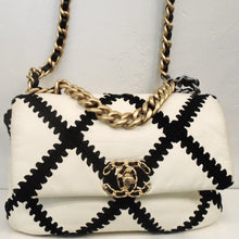 Load image into Gallery viewer, This Chanel Vintage  19  Two Tone Cotton &amp; Leather Bag has black strips of fabric with chevron edges in the chevron design on the bag. The bag is white and has three tone gold hardware. It has the double C chanel logo in gold on the front center of the bag. There is a pocket on the outside back of the bag and the interior is white.
