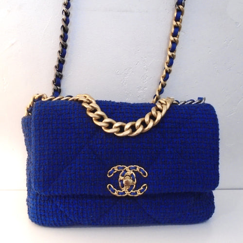 This Chanel Vintage 19 Cobalt Tweed bag has gold hardware including the chanel logo which also has blue threaded through the double Cs. The gold shoulder chain has a thin strip of blue leather woven between the links of the chain. There is an outside back pocket and the interior is blue.