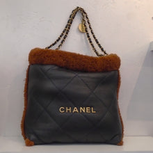 Load image into Gallery viewer, This Chanel Vintage 22 Hobo W/Shearling Trim (Shearling Pochette Included) is black with brown shearling trim and also shearling interior. The bag is in large stitched diamond pattern. It has the name Chanel in gold on the front of the bag, has double carrying chains and has a medallion attached to the carrying chain. The medallion has the words Chanel and Paris written on it along with the Chanel Logo.
