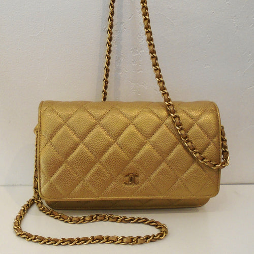 This Chanel Vintage Gold Caviar Leather WOC has the Chanel diamond stitched pattern with a small Chanel logo on the front bottom center of the front flap. It has  a gold toned hardware shoulder chain with a gold leather strip woven between the links. The inside flap has a zippered pocket and the inside of the bag has credit card pockets. The outside back of the bag has a pocket.