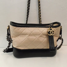 Load image into Gallery viewer, This Chanel Vintage Aged Calfskin small Gabrielle Hobo Bag is cream brown with black trim. It has a gold shoulder chain with a black leather strip woven in the chain. It has a gold logo CC attached to the zipper strip and the interior of this bag is Burgundy.
