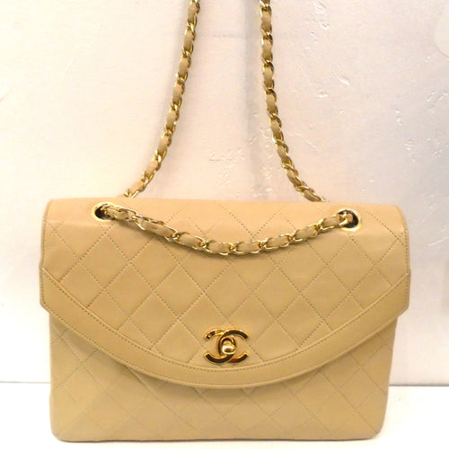 This Chanel Beige Diana Flap Bag has 24 Karat gold plated hardware and the bag is in the stitched diamond pattern. It has a gold shoulder chain with a strip of beige leather  woven between the links of the chain. The interior of the bag is also beige with a zippered pocket along with a non zippered pocket.