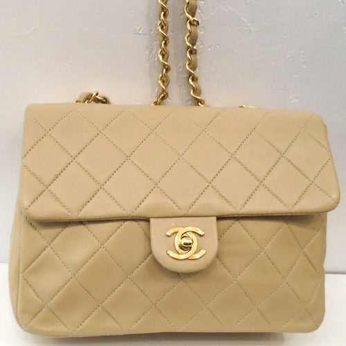This Chanel Vintage Beige Single Flap 20 Lambskin bag has the diamond stitched pattern with 24 Karat Gold Hardware. It has a long gold shoulder chain with a strip of leather woven between the links. The CC logo  front latch is in gold hardware. The inside of this bag is beige also with a pocket.