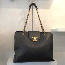 Load image into Gallery viewer, This Chanel Vintage Extra Large Weekender Tote has a diamond stitched pattern and gold hardware. This bag is also called Supermodel Tote because a lot of models use this as an overnight bag. It has a double gold shoulder chain with a thin piece of black leather woven between the links of the chain. The interior of this bag is black and has three sections which includes a middle zippered section with two pocket sections on either side.
