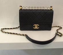 Load image into Gallery viewer, This Chanel Vintage Flap With Acrylic Beads has a row of clear acrylic beads on top of the bag with Chanel spelled out through the beads in gold. It has a short front flap with the CC logo in gold on the lip. The shoulder chain has a black strip of leather woven through it and a black shoulder guard. The interior of this bag is beige.
