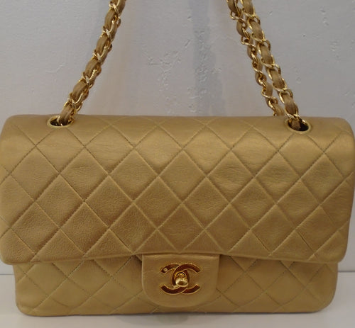 This Chanel Gold Double Flap 25 is 24 Karat Gold plated. The color of the bag is gold and it has a strip of gold leather woven between the gold chain links. This bag has an outside back pocket, gold interior and an inside pocket.