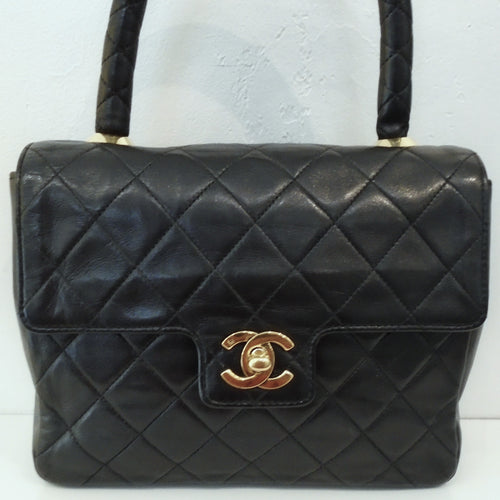 This Chanel Lambskin Top Handle is black with 24 Karat Gold Hardware which includes the Chanel Logo on the front lip of the bag. The interior is red with a zippered pocket.