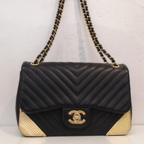 This Chanel Vintage Mini Crossbody (Rock The Corner) is black with the chevron design. It has gold toned hardware which includes the Chanel Logo latch, the front corners of the bag and the double shoulder chain. The shoulder chain also has a thin strip of black leather woven between the links of the chain. The interior of this bag is gray.