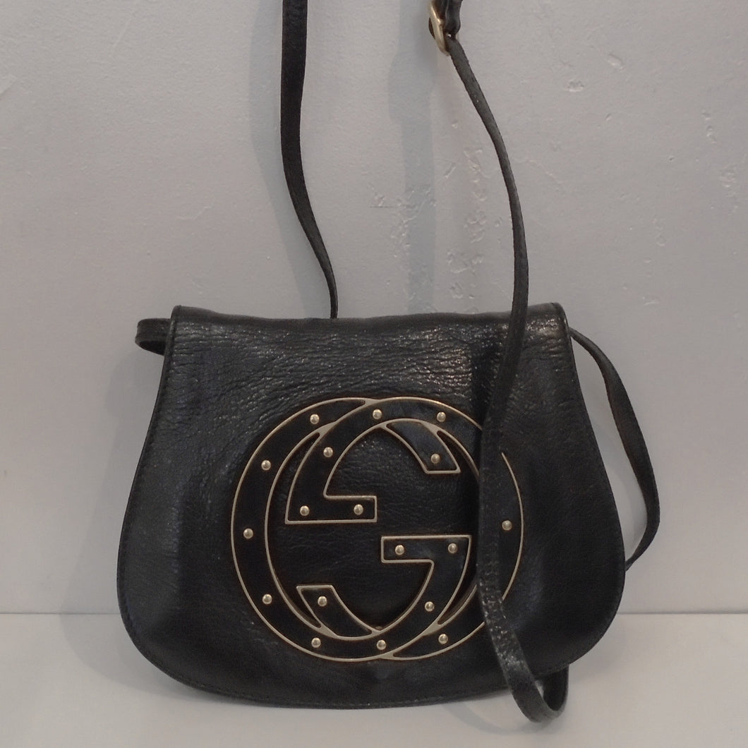 This Gucci Vintage Blondie Leather Bag is black with a large Gucci logo with inlaid leather edged in gold hardware. It has a detachable shoulder strap and the interior is black with a zippered section.
