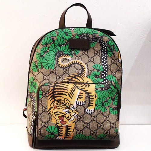 This Gucci Vintage Bengal Tiger Back Pack has an intricately stitched Bengal tiger with his mouth open along with stitched greenery on it. The bag has a front zippered pouch with sections inside. It has double zippers that meet at the top. The back straps a red and black. The interior is a beige color and has a pocket.