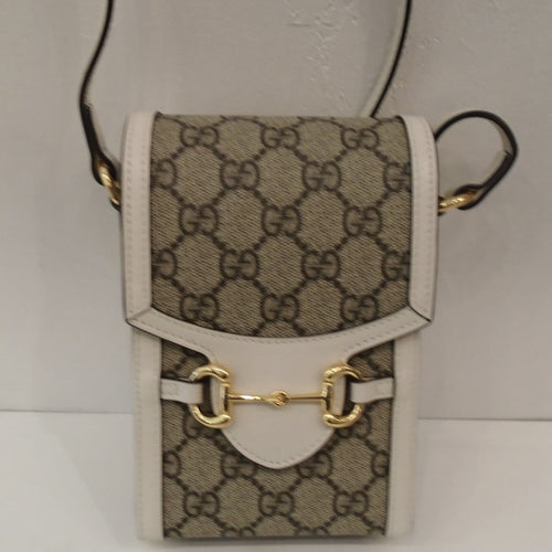 This Gucci Vintage Cream/Snaffle Crossbody is in the Gucci pattern in cream trim with a tongue on the front flap. It has a gold hardware snaffle across the tongue to hold the crossbody closed. It has a cream leather adjustable shoulder strap. The interior of this bag is a light brown.
