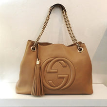 Load image into Gallery viewer, This Gucci Vintage Camel Soho Tote has the Gucci Logo in large raised letters stitched into the front of the bag. It has a tassel that hangs to the bottom of the bag made from the same material as the bag. It has a double shoulder chain with a shoulder guard. The interior of this bag is pink with a soft white lining.
