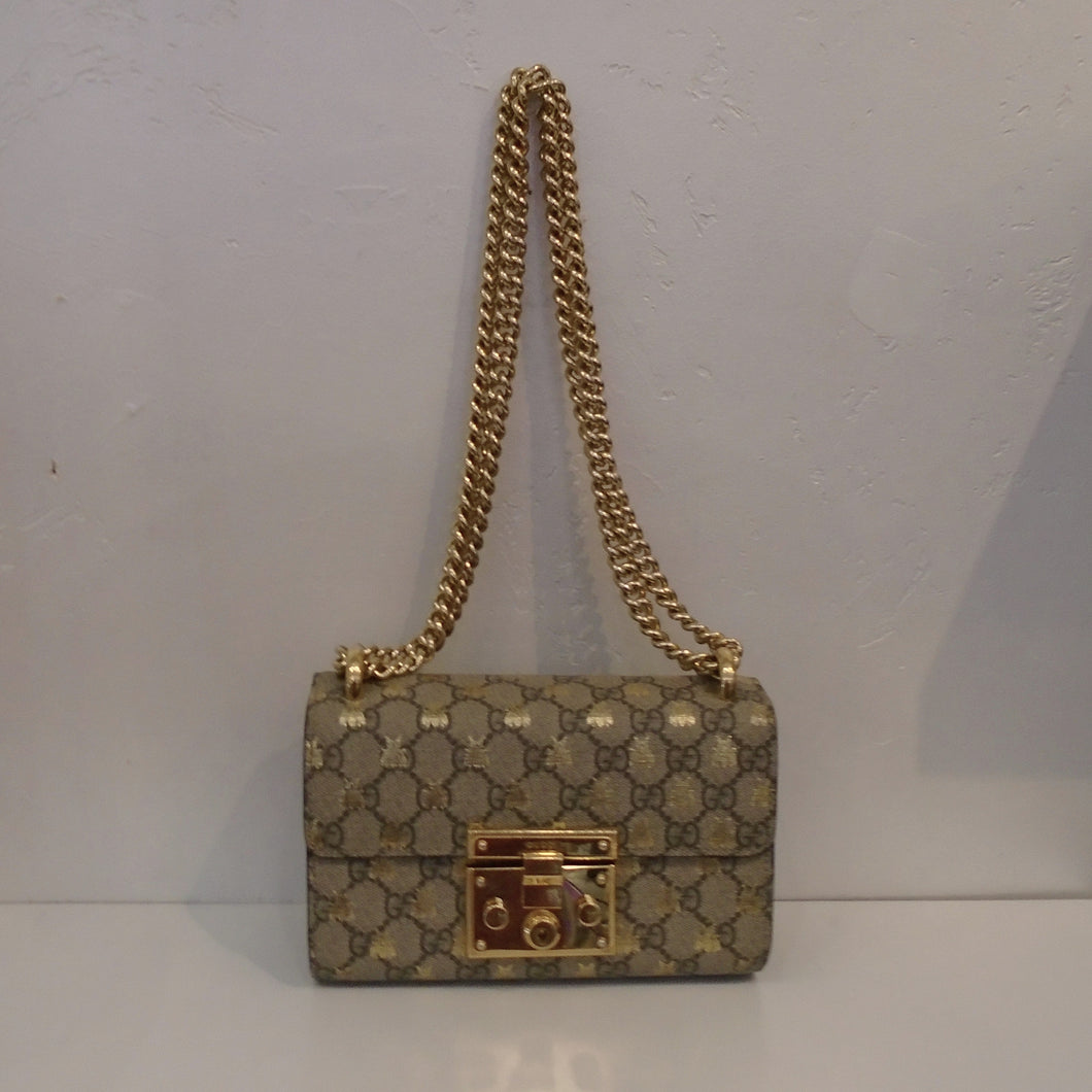 This Gucci Vintage Guccissima Small Gold Bee Padlock 2 Way Bag is in the Gucci pattern with golden bees withing the pattern. It has a gold front latch and double gold shoulder chain. It has a black back pocket and the interior is gold.