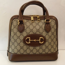Load image into Gallery viewer, This Gucci Mini 1955 Horsebit Top Handle  bag has a gold horsebit on a brown leather oval on the center of the bag. It is trimmed in brown leather with double carrying handles. This bag has a gold zipper opening and the two zipper pulls meet at the top of the bag.
