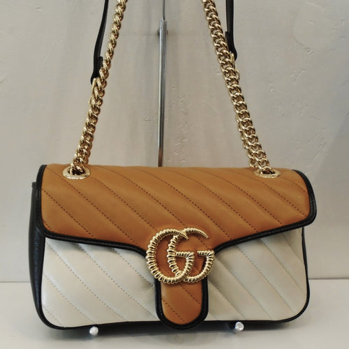 This Gucci Vintage Maramont Multicolor bag has a double gold chain with a black leather section on one end. The bag is in the colors of camel, cream and black with black trim. The gold Gucci logo initials on the front of the bag are grooved giving it a 