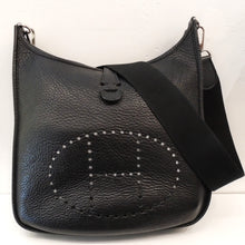 Load image into Gallery viewer, This Hermes Black Evelyne Clemence Leather PM has silver hardware and a wide sturdy canvas shoulder strap. It has a small strap at the top of the bag that pulls the top together, a pocket in the back that also has a  strap snap closure. The interior of the bag is the inner side of the leather. This bag is somewhat soft with a pebbled appearance.
