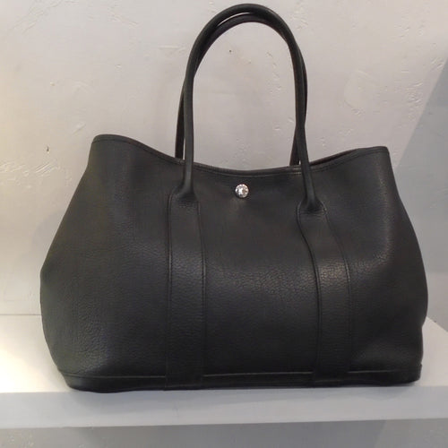 This Hermes Vintage Black Garden Party Togo Leather bag has double carrying handles large enough to use as a shoulder bag. It has a silver snap to close the bag with Hermes Paris engraved on it. The interior is tan with a black bottom. It also has a zipper inside the bag.