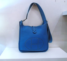 Load image into Gallery viewer, This Hermes Vintage Evelyne PM Blue Clemence Leather is a dark sky shade of blue. It has the perforated &quot;H&quot; on the front of the bag. The top is held together with a thin strap from the back that slips through a loop on the front. The hardware of this bag is silver.

