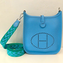 Load image into Gallery viewer, This Evelyne  Hermes TPM Clements Leather bag is a sky blue color with the Hermes logo perforated on the center bottom of the bag. It has a green and sky blue zig zag design guitar strap carrying handle.  The interior is also sky blue.

