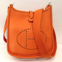 Load image into Gallery viewer, This Herm`es Vintage Evelyne TPM Orange Clemence Leather Bag has the Herm`es logo hole punched in the front of the bag. It has silver hardware.
