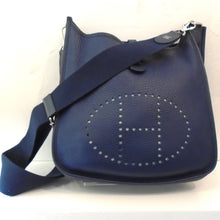 Load image into Gallery viewer, This Herm`es Navy Evelyne III Generation PM is navy blue with the Hermes logo hole punched on the front of the bag. It has the original guitar strap included and has silver hardware.
