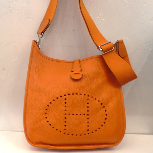 This Hermes Vintage Orange Clemence Leather Evelyn PM has silver hardware and the sturdy canvas (guitar strap) shoulder strap. The front of the bag has the Hermes Logo perforations.