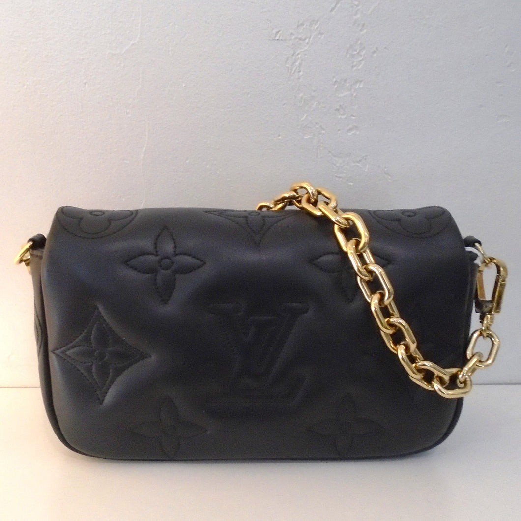 This Louis Vuitton Vintage Black Bubblegram Wallet has large embossed monogram. It has gold hardware which includes a heavy chain which is detachable. It also includes a guitar strap which is also detachable. The interior of this bag is black.