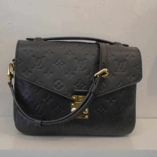 This Louis Vuitton Black Empreinte Leather Metis Pochette is imprinted with the regular size monogram. It has gold hardware, a carrying handle and shoulder strap. This bag has a back outside zipper and the interior is a light brown with dark brown stripes. 