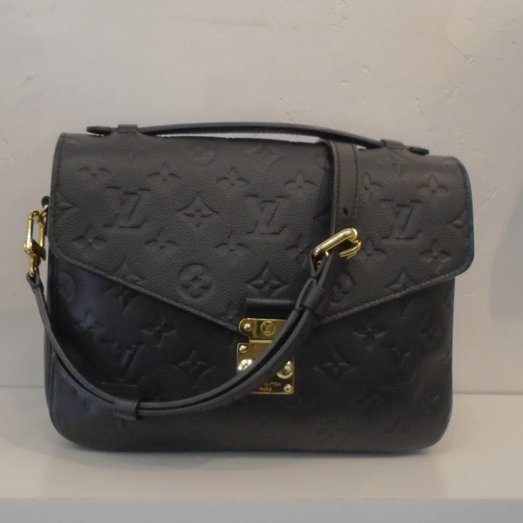This Louis Vuitton Black Empreinte Leather Metis Pochette is imprinted with the regular size monogram. It has gold hardware, a carrying handle and shoulder strap. This bag has a back outside zipper and the interior is a light brown with dark brown stripes. 