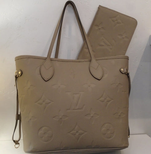 This Louis Vuitton Vintage Neverfull Empreinte Leather MM With Pochette is beige with the large Monogram embossed in the leather on both the bag and pochette. The bag has cinch sides and the interior is brown.