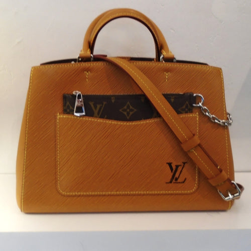 This Louis Vuitton Vintage Cognac Epi Marelle Tote is in the color Cognac which is a golden brown. It has a large center front pocket on the outside of the bag which has the Louis Vuitton Logo in the lower right corner of the pocket. There is a pochette sitting in the pocket which is in the original monogram pattern and is attached by a silver chain. The interior of this bag is dark brown.