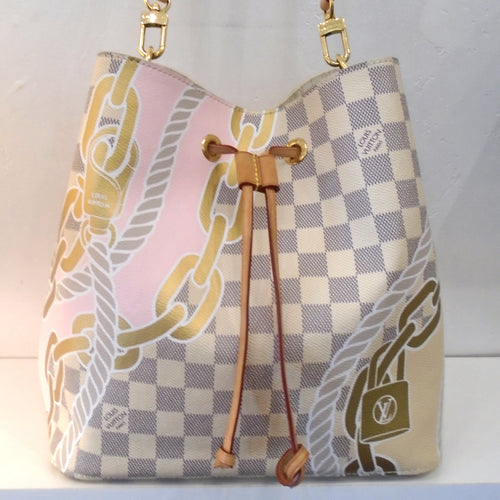 This Louis Vuitton Vintage Damier Azur Nautical Neo Noe is gray and white damier azur with nautical rope, chains and lock printed on the bag. It has a camel leather drawstring, gold hardware and a leather shoulder strap. The interior of the bag is a cream color with monogram design in gray and has a damier azr zippered pouch.