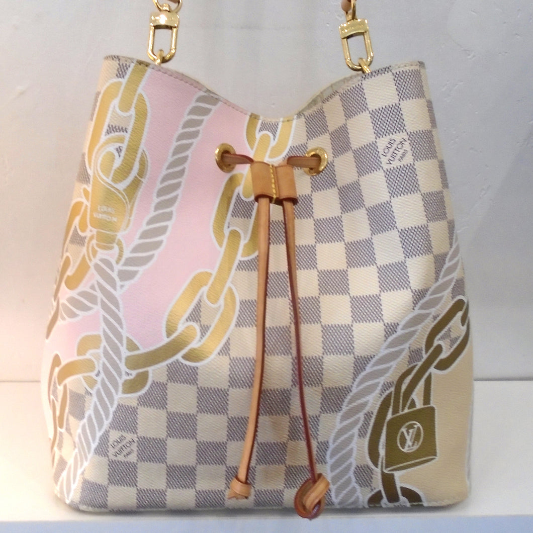 This Louis Vuitton Vintage Damier Azur Nautical Neo Noe is gray and white damier azur with nautical rope, chains and lock printed on the bag. It has a camel leather drawstring, gold hardware and a leather shoulder strap. The interior of the bag is a cream color with monogram design in gray and has a damier azr zippered pouch.