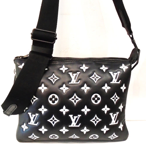 This Louis Vuitton Vintage Lambskin Monogram Coussin PM is black with Large white Monogram imprinted in the leather. It has a sturdy black adjustable guitar strap/shoulder strap. The bag is in three sections and has a burnt orange interior.