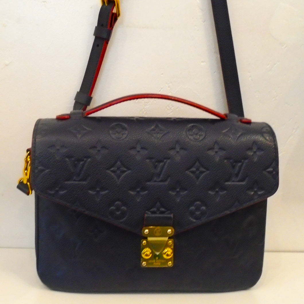 This Louis Vuitton Vintage Navy Metis Burgundy Trimmed Pochette has gold hardware, a carrying handle and an adjustable shoulder strap. The interior of this bag is red with black stripes.