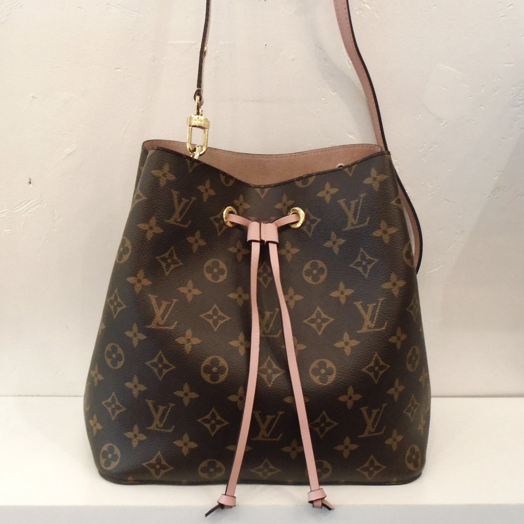 This Louis Vuitton Vintage Monogram NeoNoe has the traditional brown monogram pattern on the outside of the bag. It has a pink leather strip for the drawstring which dangles down the front of the bag knotted at the ends.  This bag has a detachable pink shoulder strap and the interior is a pink mauve shade.