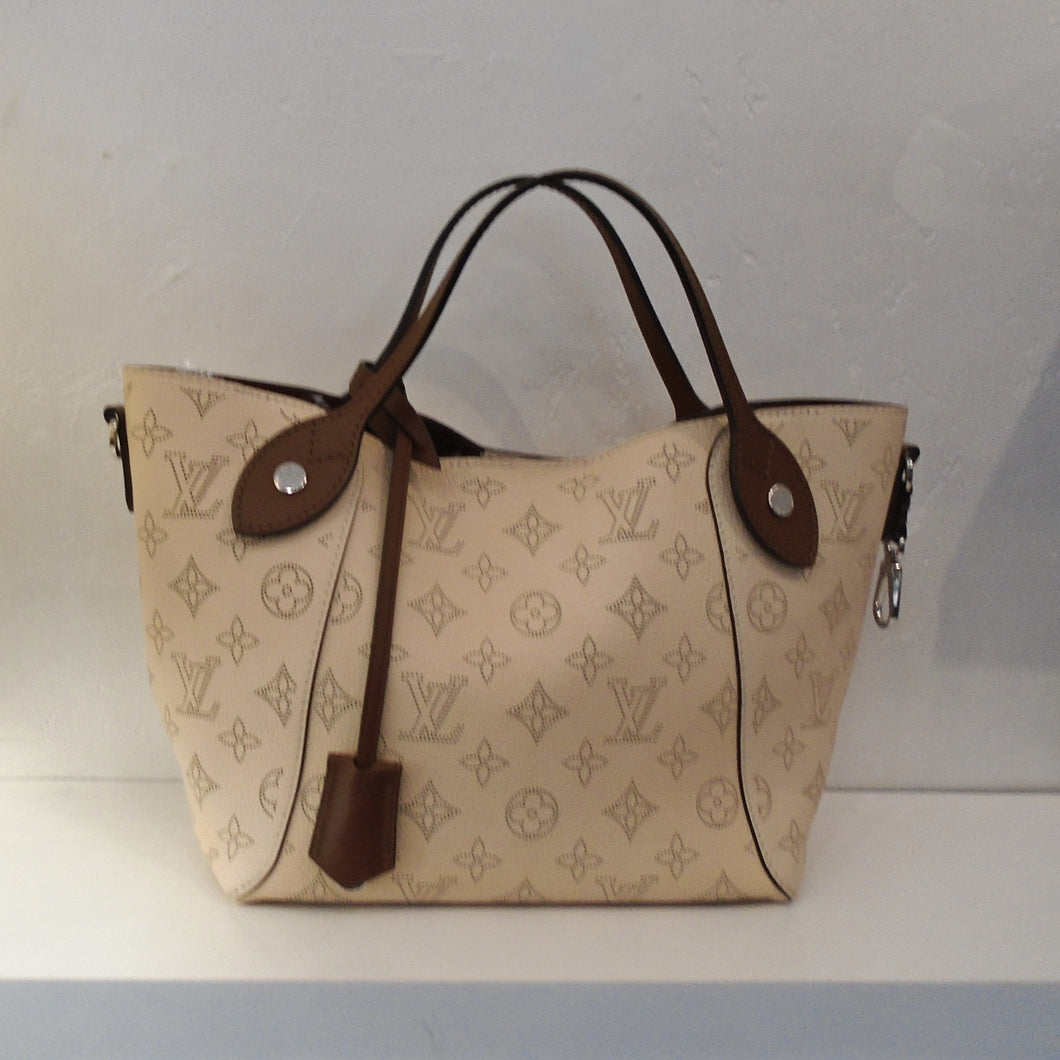 This Louis Vuitton Vintage Mahina Hina PM is beige with large beige monogram and dark brown trim which includes the carrying handles.  The interior is dark brown with a white bottom. It also has a detachable shoulder strap.
